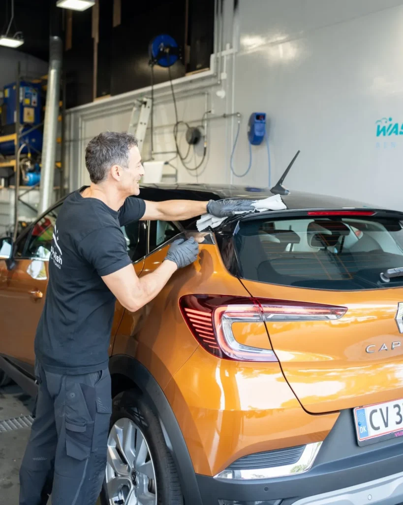 Medarbejder aftørrer en orange bil efter vask